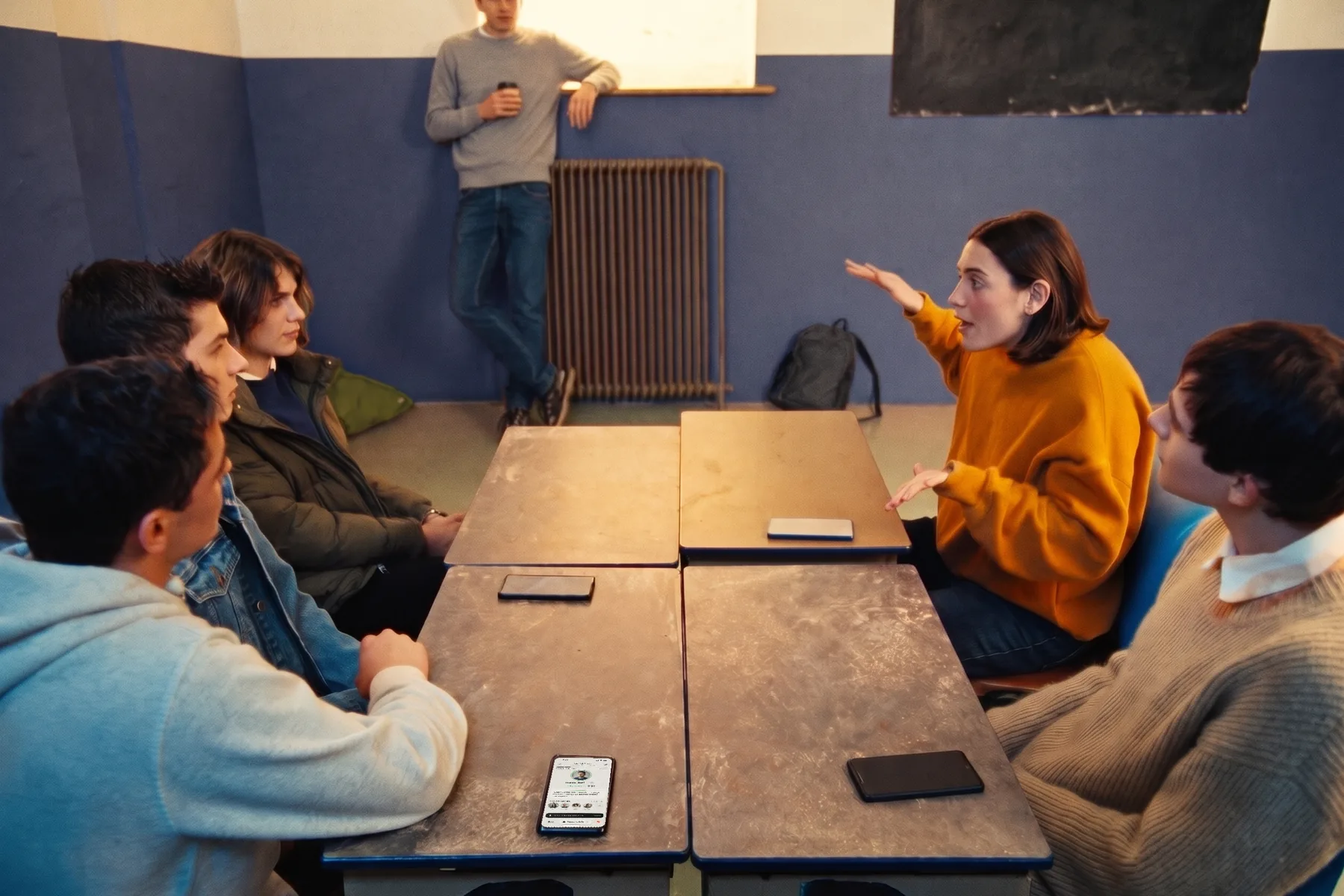 Six students around two desks pushed together: a girl is speaking, the others listen
